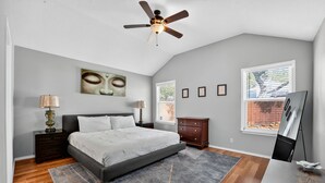 Ein Schlafzimmer mit Bett, Nachttischen, Deckenventilator, Fenster und Kunstwerk an der Wand.
