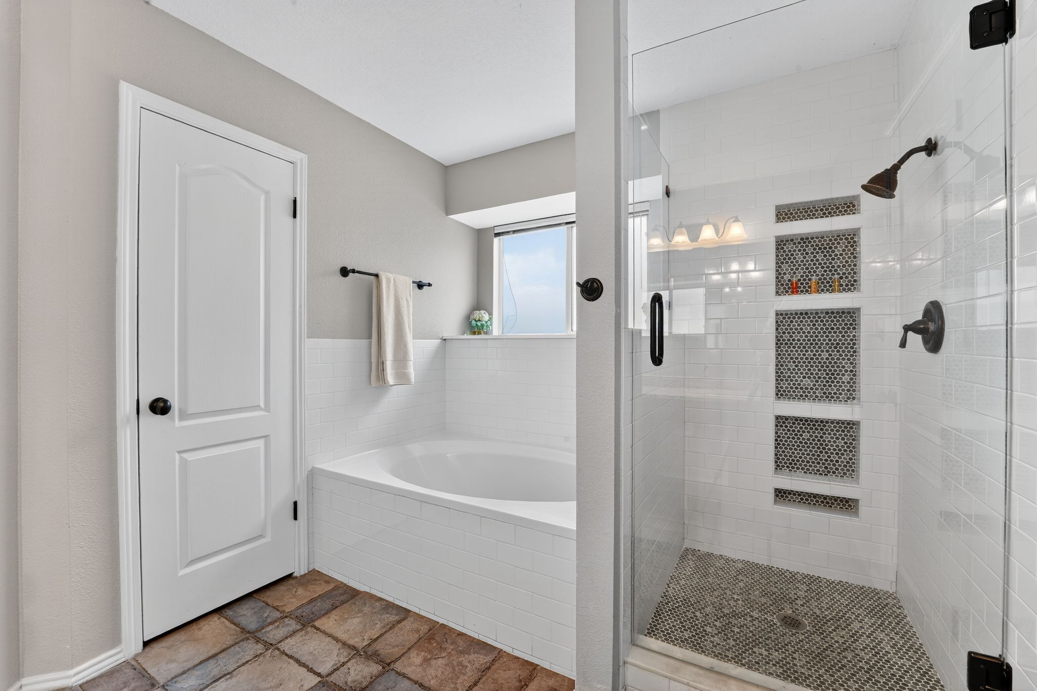 Un baño moderno con una bañera blanca, una ducha con cerramiento de vidrio y un pequeño ventanal sobre el lavabo.