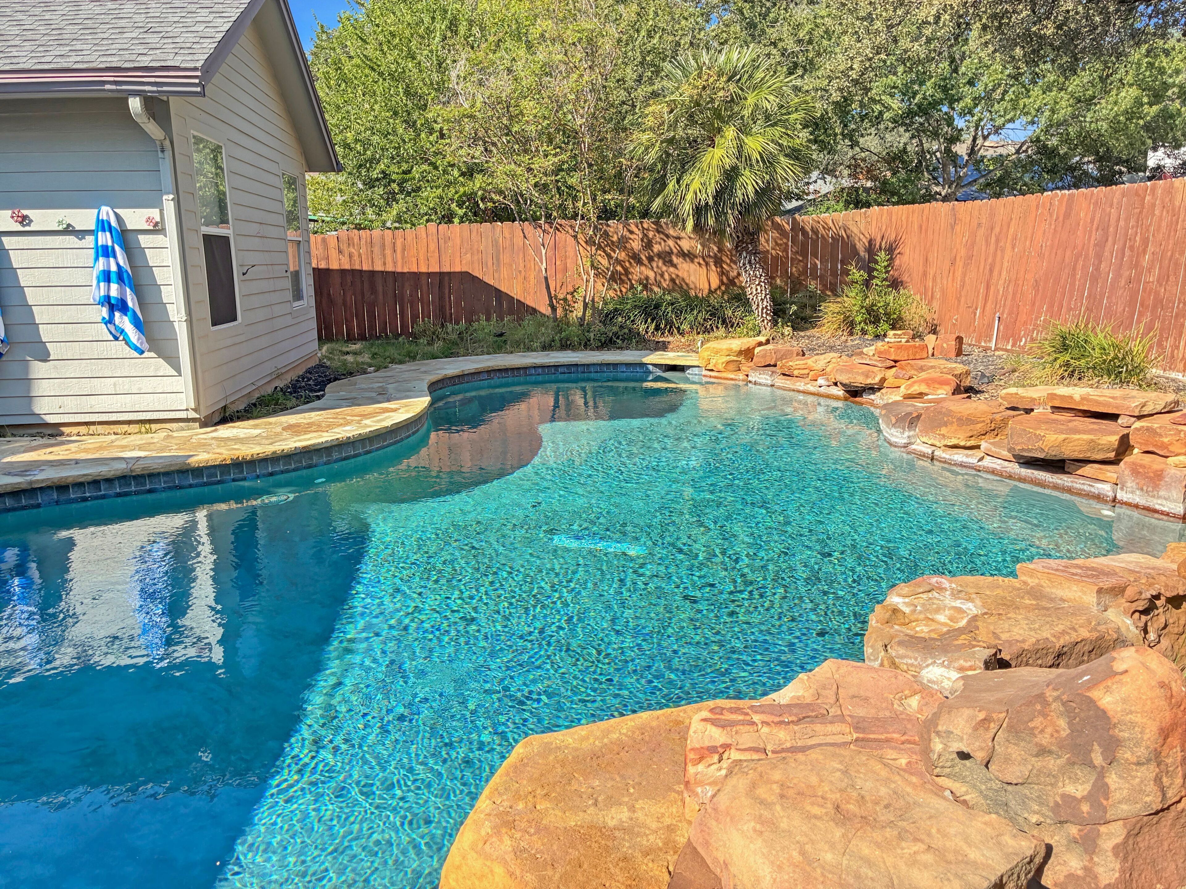 Une piscine aux eaux cristallines, avec une terrasse en bois et un petit bâtiment situé à gauche.