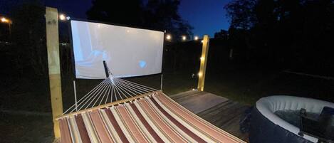 Un cinéma en plein air doté d’un grand écran, d’un sol à rayures et d’une piscine.