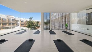 Un balcon spacieux agrémenté de tapis noirs disposés pour la pratique du yoga, offrant une vue sur les bâtiments et agrémenté d’un paravent vertical en bambou.