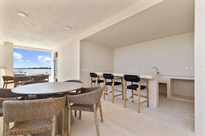 A modern kitchen with a dining area, featuring a round table and wicker chairs, and a view of the sea. - Cozy Getaway w Private Plunge (Tulum Municipality)