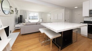 A modern kitchen with a large island, white cabinetry, and a dining area with a sofa and bench. - Modern Retreat w/ Fire Pit & Parking (Annapolis)