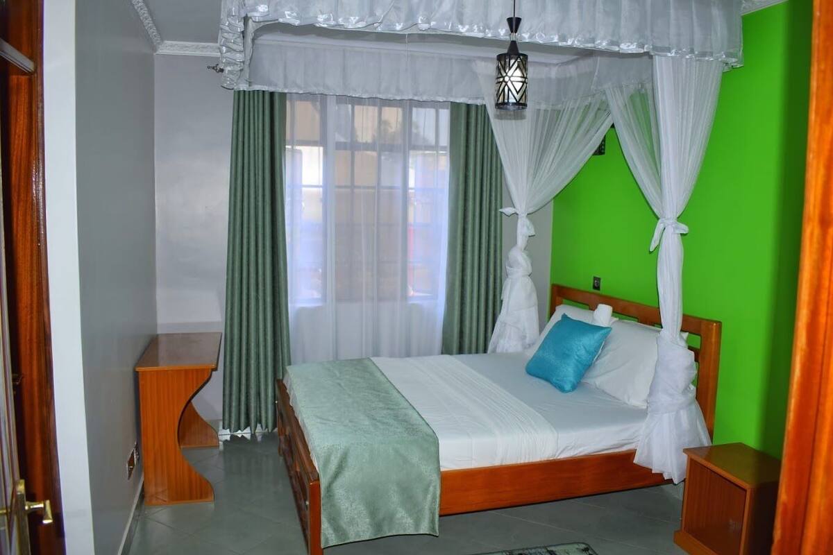 A bedroom with a wooden bed, green curtains, a white canopy, and a green wall.