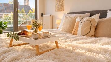 A bedroom with a fluffy white carpet, a bedside table with a tray of breakfast items, and a view of a building through the window.