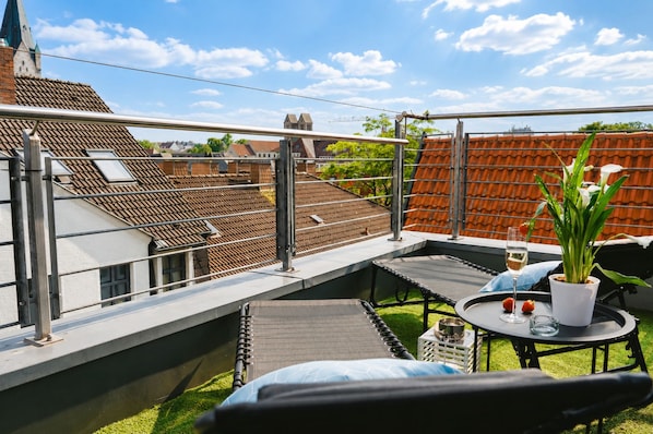 A rooftop terrace with a seating area, a potted plant, and a glass of wine.
