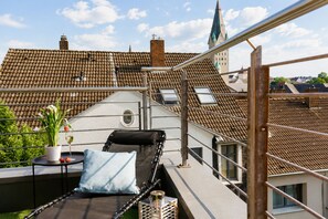 Une terrasse sur le toit, avec un fauteuil de relaxation, une petite table agrémentée d’une plante en pot et un verre de vin, et une vue sur le paysage urbain.