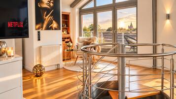 A modern living room with a spiral staircase, a large window with a city view, a fireplace, and a Netflix poster.
