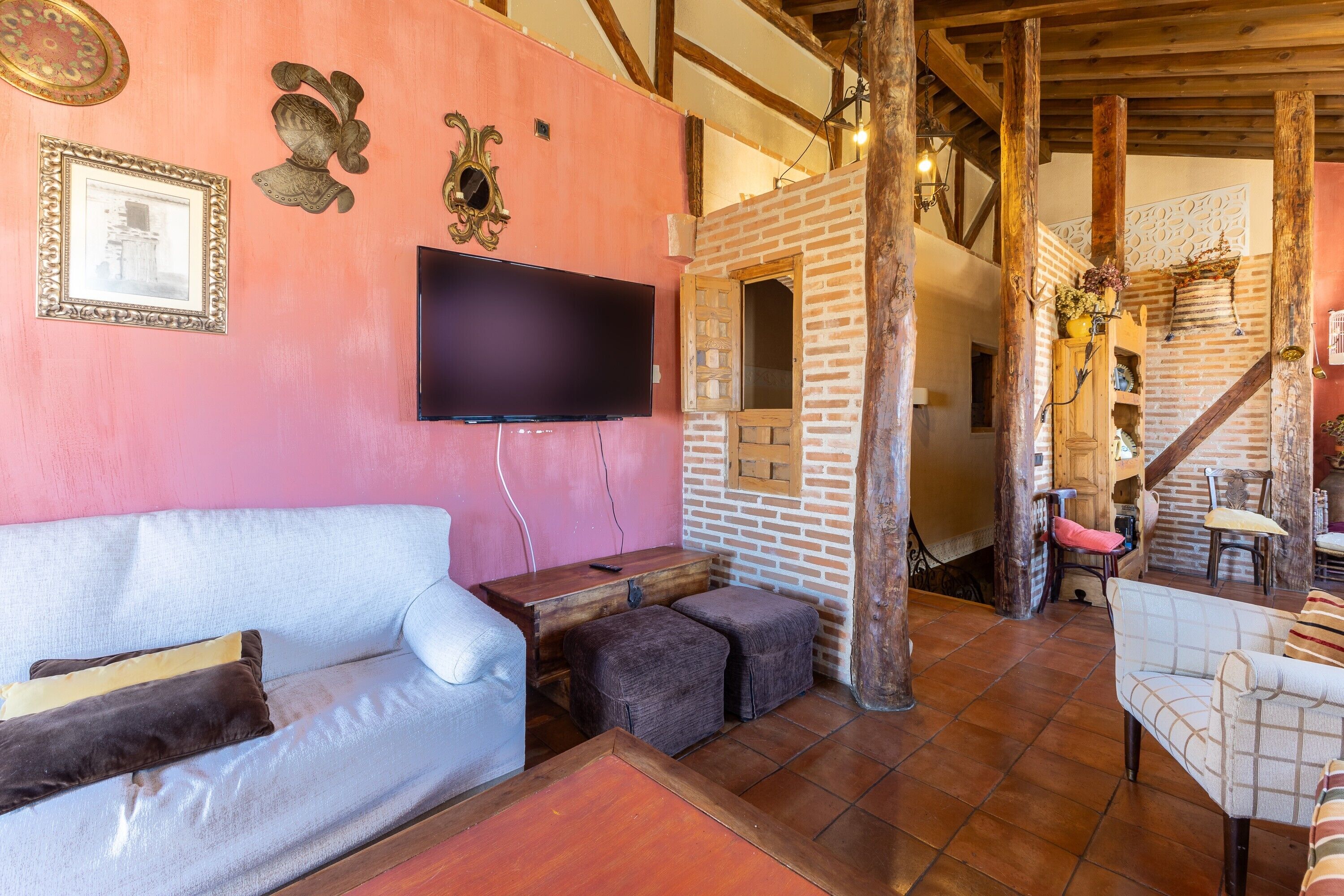 A cozy living area with a sofa, ottomans, a flat-screen TV, and a brick wall.