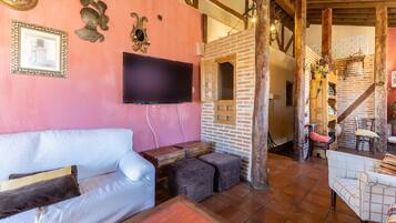 A cozy living area with a sofa, ottomans, a flat-screen TV, and a brick wall.