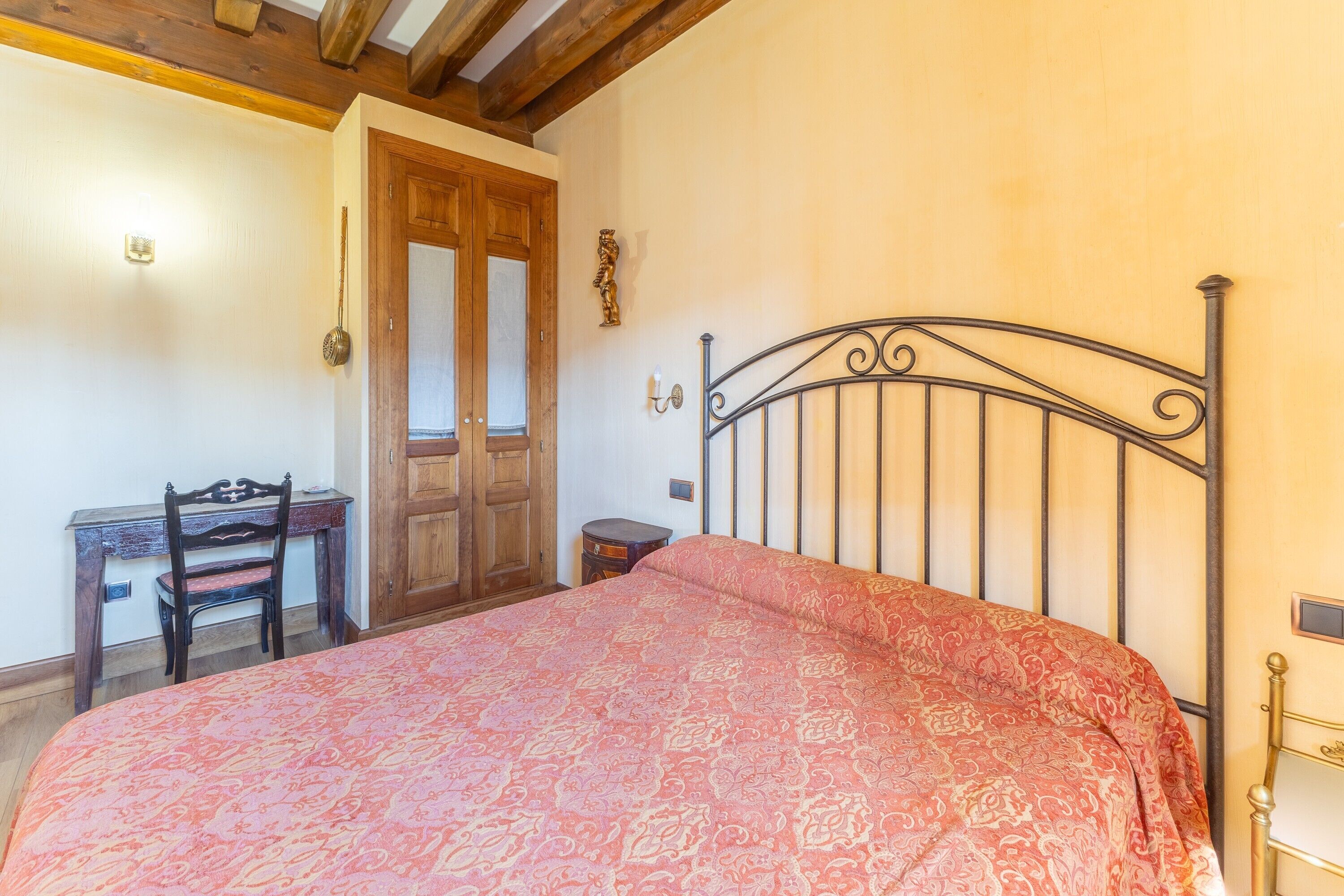 A bedroom with a bed, wooden desk, chair, and a door.