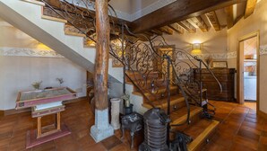 Un escalier orné de rampes en métal ouvragé, une colonne en bois et une table en verre agrémentée d’objets décoratifs.