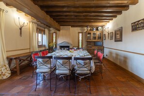 A dining area with a long table set for a meal, wooden beams on the ceiling, and a fireplace.
