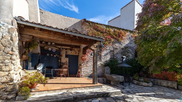 Un bâtiment en pierre agrémenté d’une pergola en bois, avec des espaces de repos en plein air et des plantes en pot.