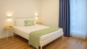 A bedroom with a bed, bedside tables, a nightstand, a window with curtains, and a wooden floor. - Magnolia Suites & Stays: Standard Suite (Porto)