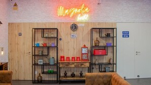 A cozy lounge area with a neon sign reading "Magnolia Hotel," wooden shelves with various items, a "NO SMOKING" sign, and a blue elevator sign. - Magnolia Suites & Stays: Standard Suite (Porto)