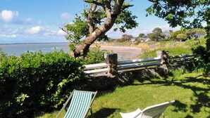 Een gazon met een houten omheining, een bank en twee streepstoelen met uitzicht op een strand.