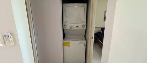 A compact laundry room with a washing machine and dryer, a small step stool, and a telephone.