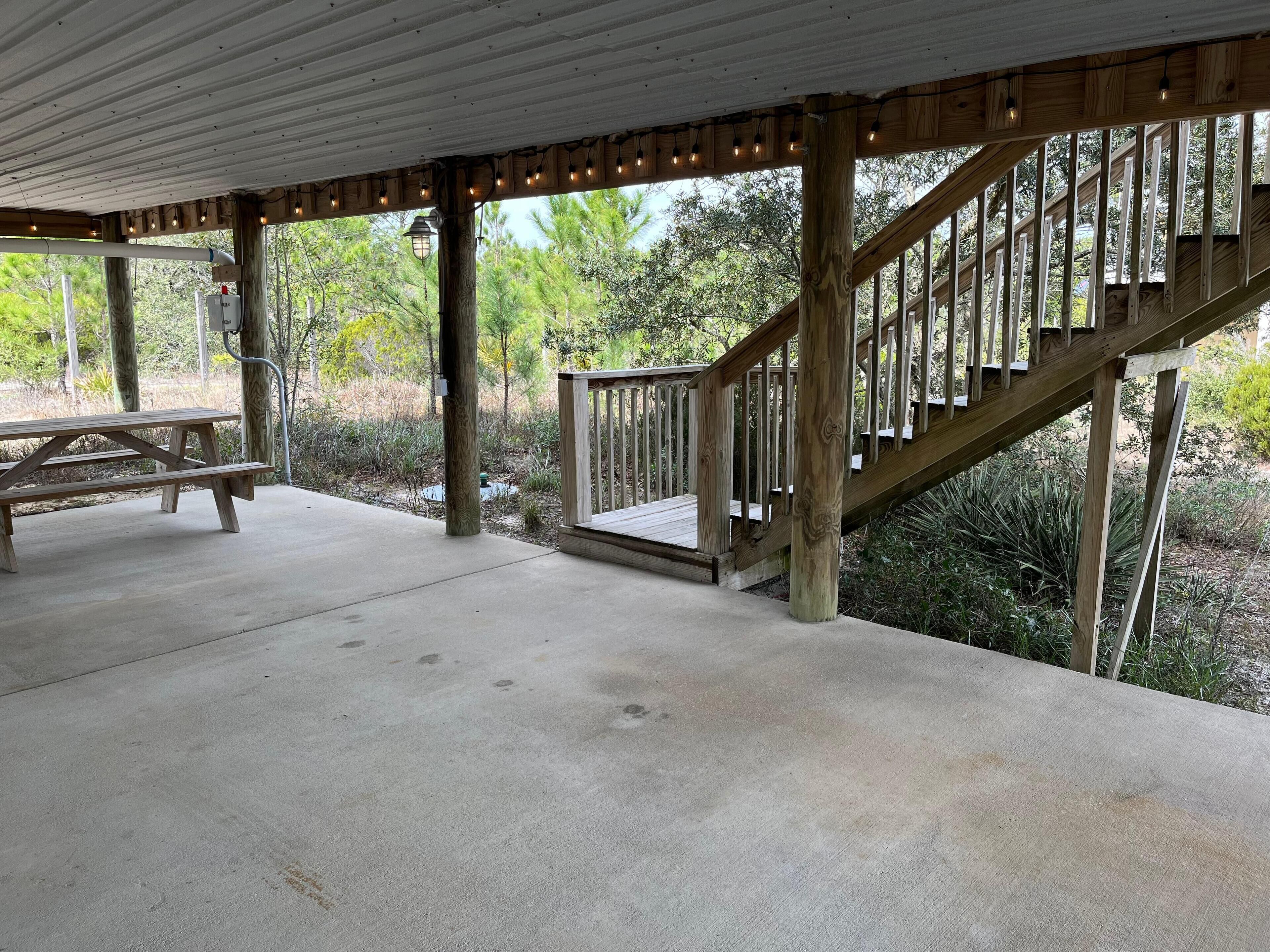 A covered outdoor area with a picnic table, wooden staircase, and a concrete floor.