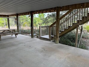 A covered outdoor area with a picnic table, wooden staircase, and a concrete floor. - Whitesands Beach House - North (Gulf Shores)