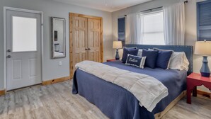 A bedroom with a bed, two nightstands, a ceiling fan, a door, and a window with curtains. - Whitesands Beach House - North (Gulf Shores)