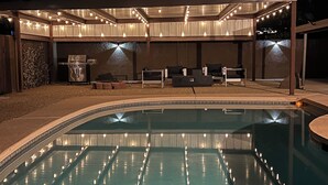 Ein Pool mit überdachter Terrasse, Sitzgelegenheiten im Freien und Lichterketten.