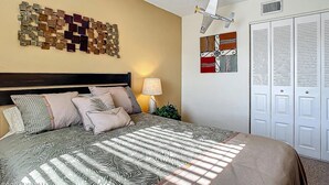 Une chambre à coucher comprenant un lit, des oreillers, une table de chevet, une lampe, un tableau décoratif et une armoire.