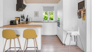 Una cocina moderna con armarios blancos, encimera de madera, dos sillas amarillas, una silla blanca y una ventana con vistas a zonas verdes.