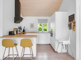 Una cocina moderna con armarios blancos, encimera de madera, dos sillas amarillas, una silla blanca y una ventana con vistas a zonas verdes.