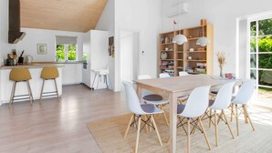 Una cocina moderna con armarios blancos, techo de madera y un comedor con una mesa grande y sillas blancas.