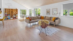 Un salón espacioso con techo alto, una amplia estantería, un conjunto de sofás y un comedor con mesa y sillas.