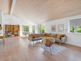 Un salón espacioso con techo alto, una amplia estantería, un conjunto de sofás y un comedor con mesa y sillas.