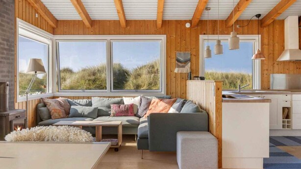 L’intérieur d’un chalet accueillant, avec un plafond en bois, de grandes fenêtres, un canapé, une petite table et un coin cuisine.