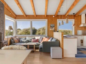 L’intérieur d’un chalet accueillant, avec un plafond en bois, de grandes fenêtres, un canapé, une petite table et un coin cuisine.