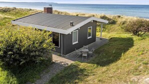 Une maison moderne avec un toit plat, une cheminée et un patio aménagé avec du mobilier d’extérieur.