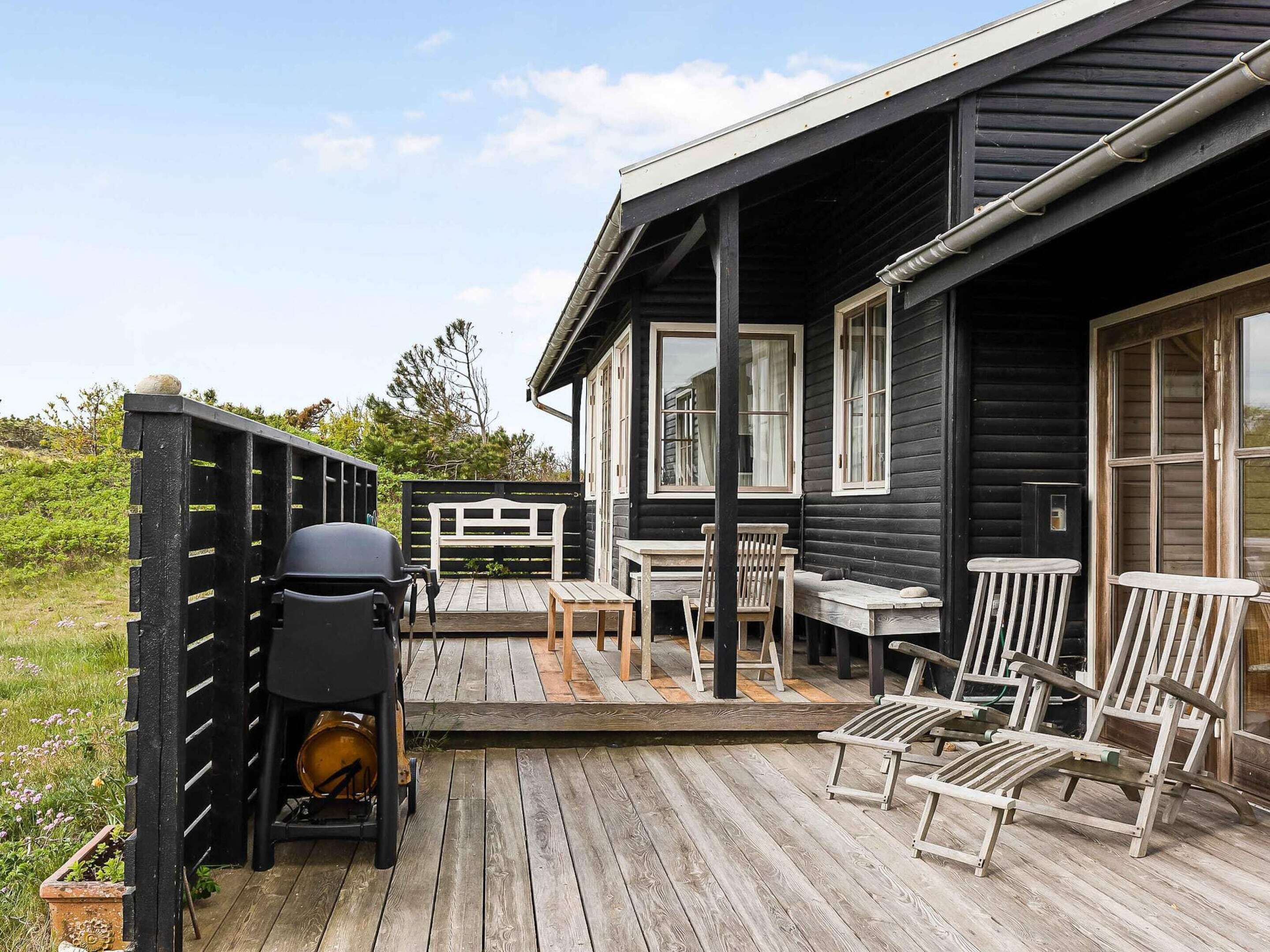 Une terrasse en bois, avec des meubles d’extérieur, un barbecue et une clôture.