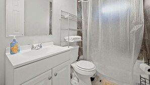 Ein Badezimmer mit Waschbecken, Spiegel und Toilette. Eine Duschvorhang und ein Handtuchhalter sind vorhanden.