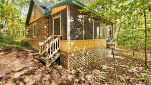A wooden cabin with a porch, surrounded by trees.