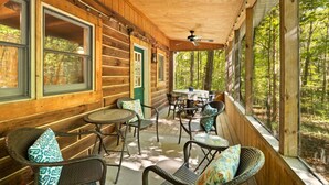 A wooden cabin with a covered porch, furnished with wicker chairs and a table.