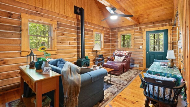 A cozy cabin interior with wooden walls, a sofa, a chair, a table, and a fireplace.