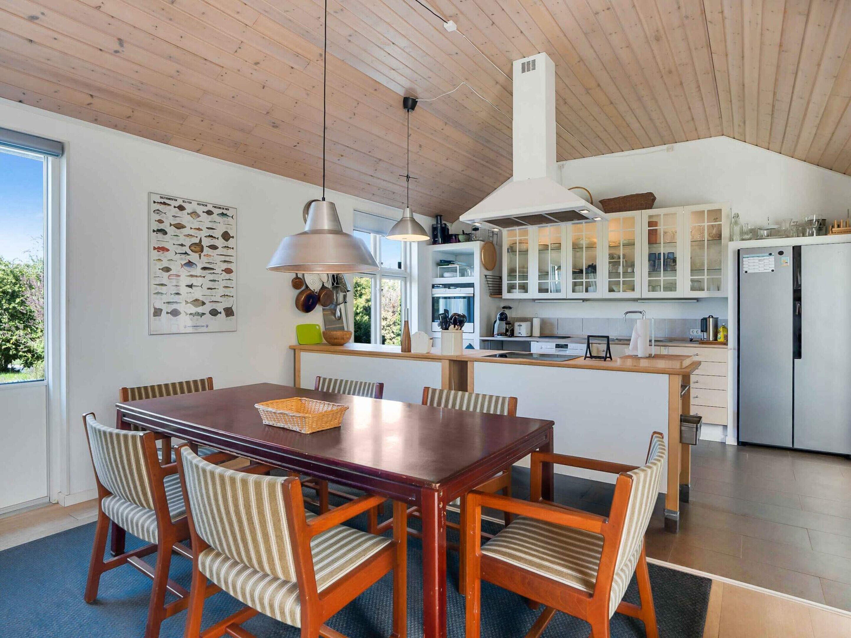 Eine moderne Küche mit Holzschränken, einem Edelstahlkühlschrank und einem Essbereich mit Holztisch und gestreiften Stühlen.