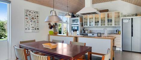 A modern kitchen with wooden cabinets, a stainless steel refrigerator, and a dining area with a wooden table and striped chairs.
