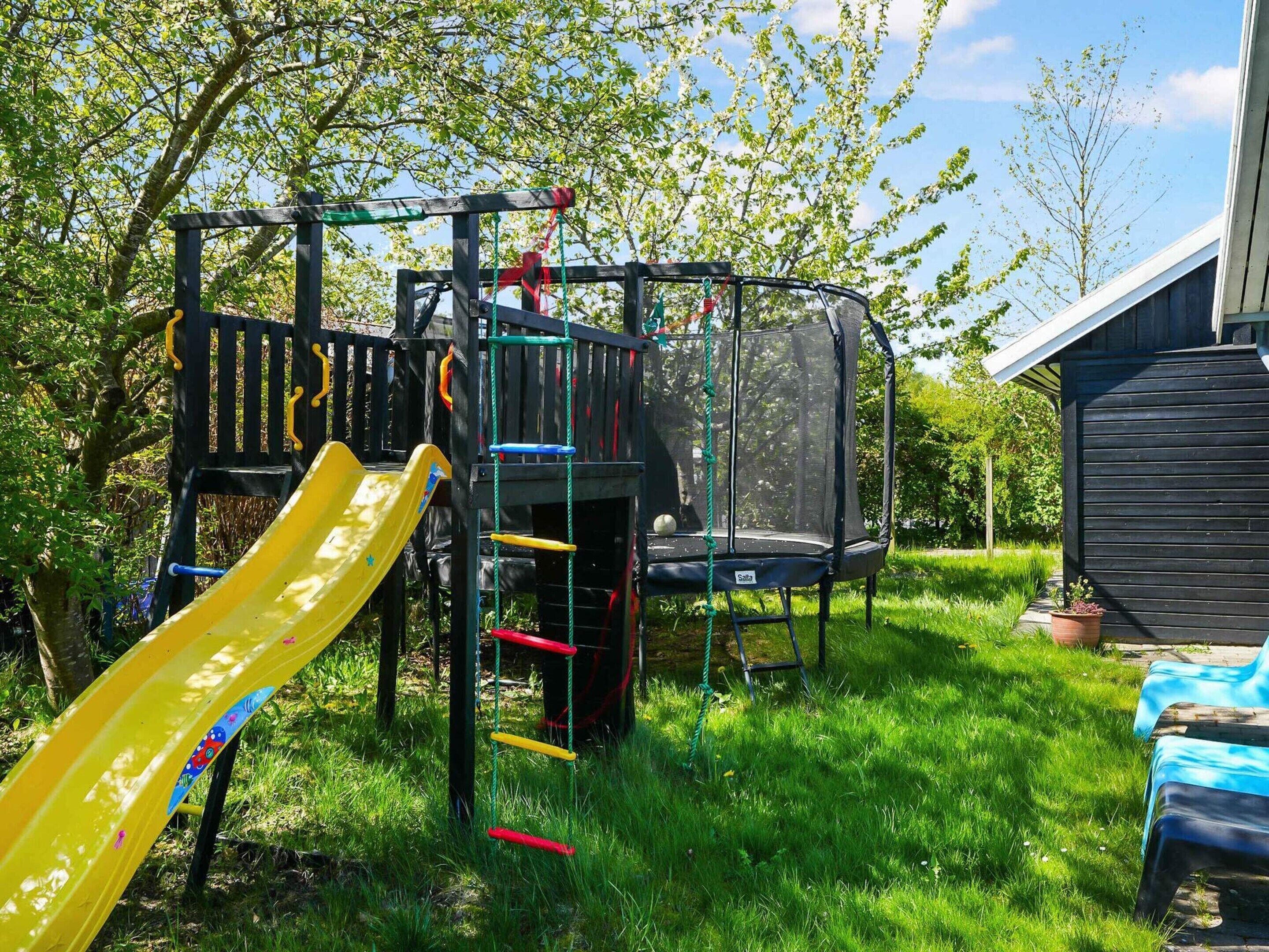 Un parque infantil con tobogán, estructura para escalar y cama elástica.