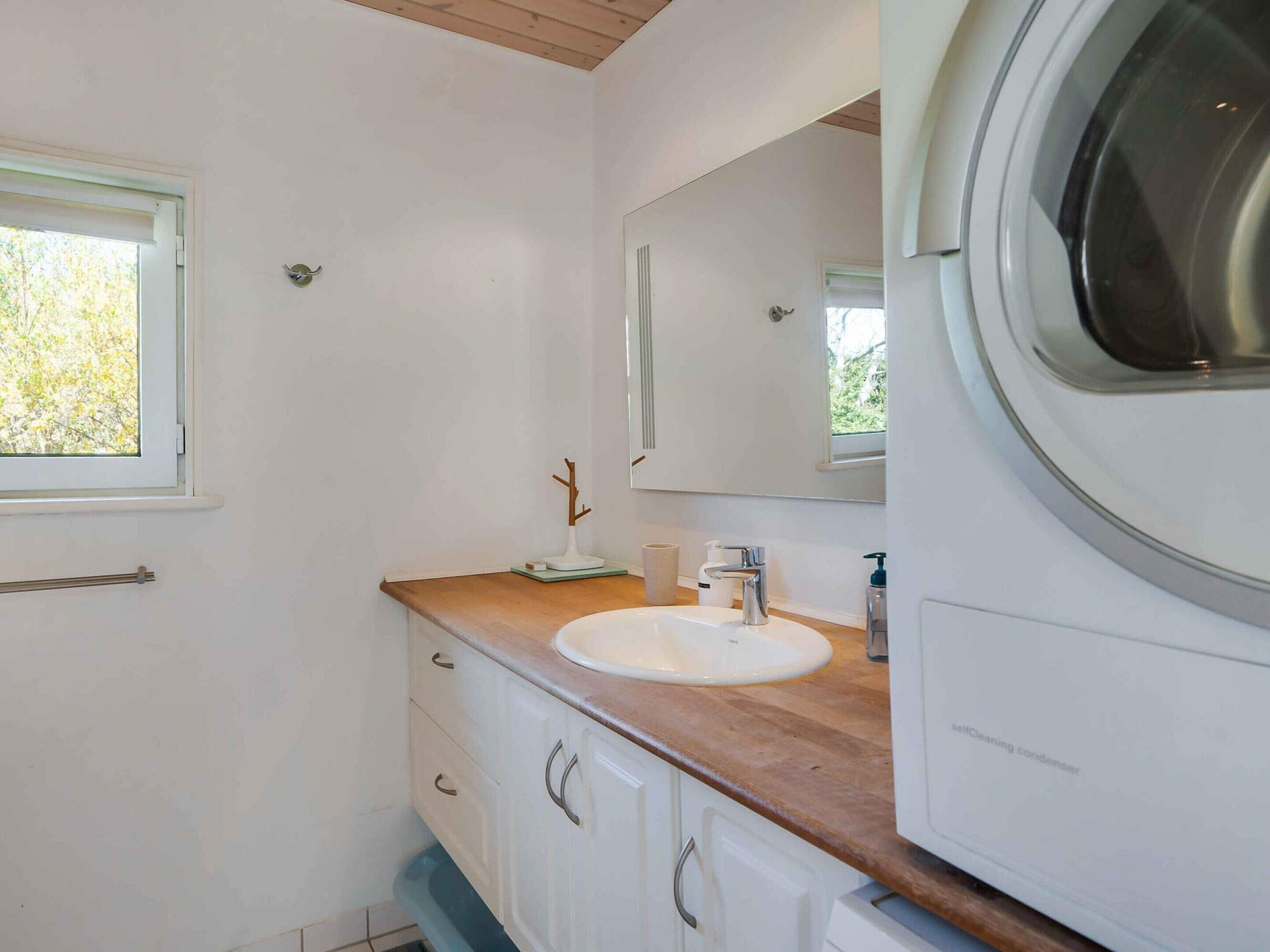 A modern bathroom with a wooden vanity, a white sink, a large mirror, and a washing machine.