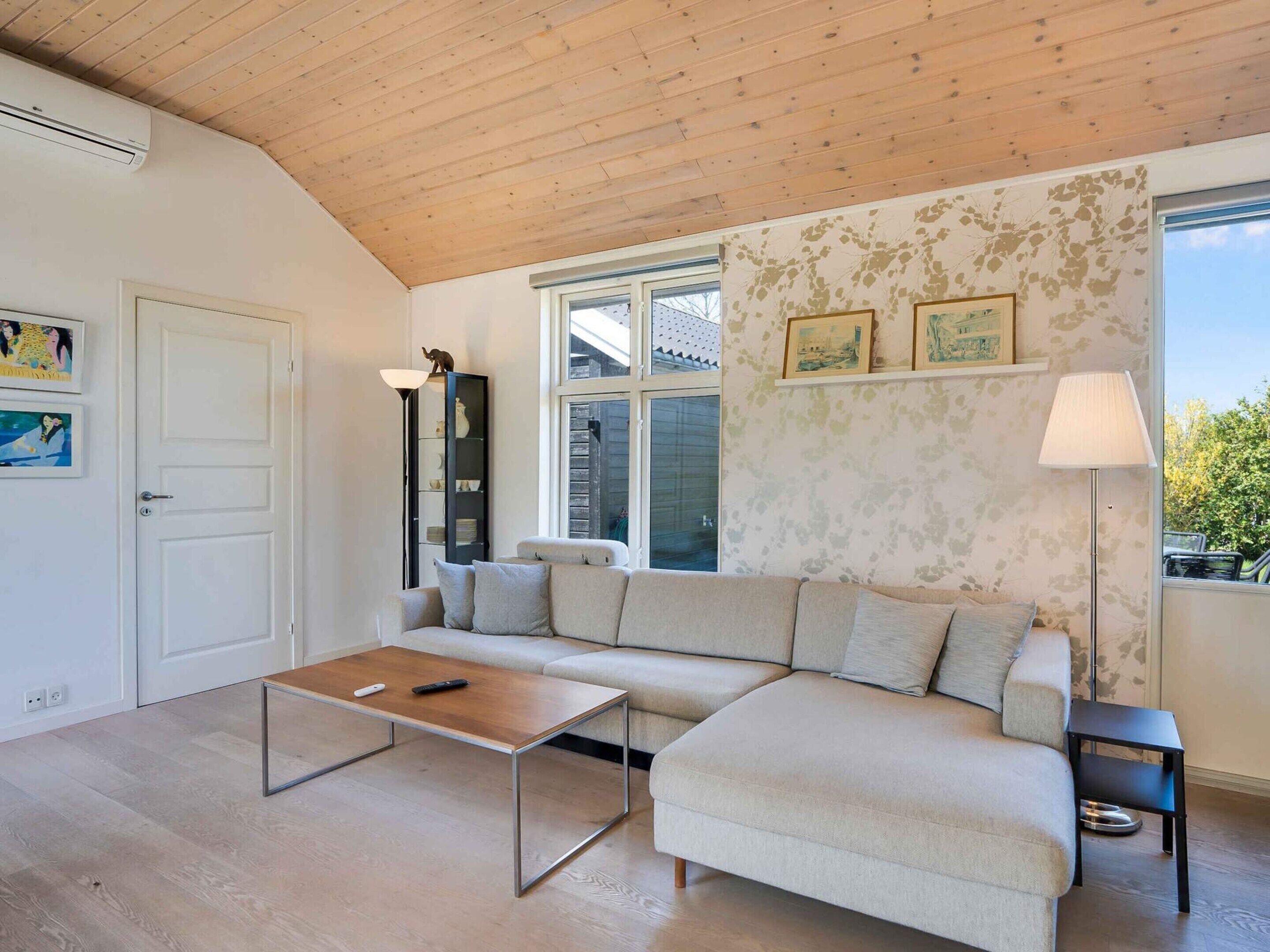 A modern living room with a wooden ceiling, a sectional sofa, a coffee table, a floor lamp, and a bookshelf.