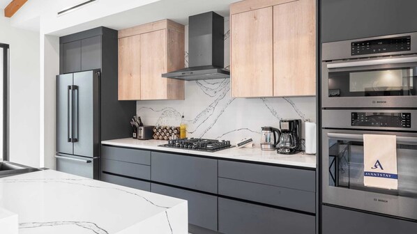 Une cuisine moderne dotée d’un réfrigérateur en acier inoxydable, d’appareils électroménagers Bosch, d’un dosseret en marbre et de meubles en bois.