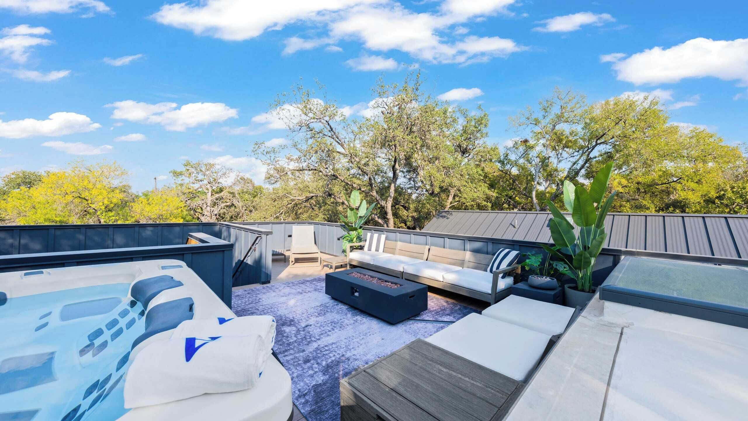 A rooftop patio with a hot tub, seating area, and potted plants.