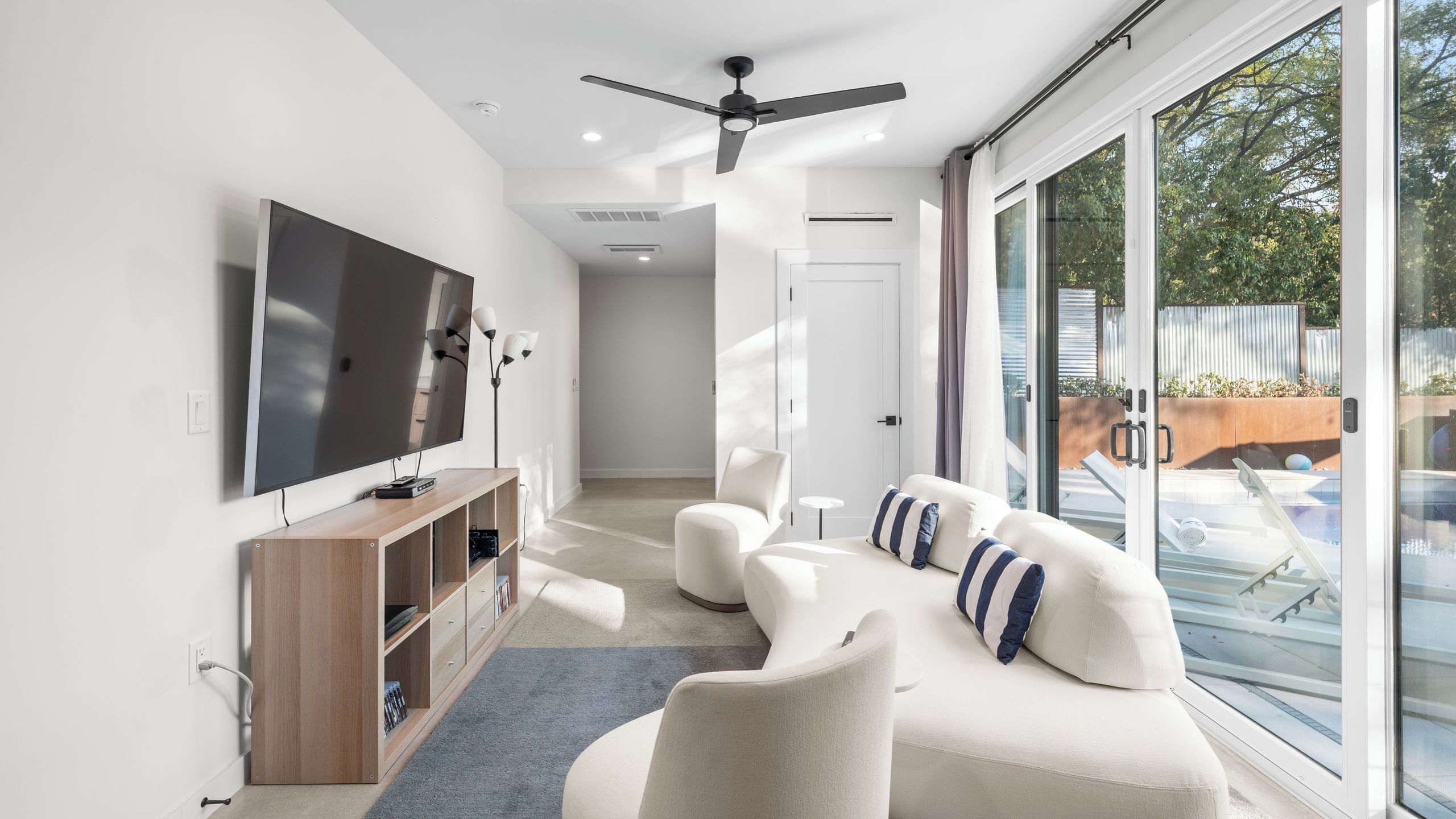Een moderne woonkamer met een flatscreen televisie, een houten tv-meubel, een witte bank en een plafondventilator.