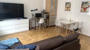 En stue med sofa, fjernsyn, spisebord med stole, et træskab og billeder i rammer på væggen.