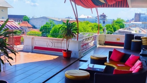 An outdoor seating area with tables and chairs, a potted plant, and a view of buildings and greenery. - Tickle Hotel (Gondokusuman)